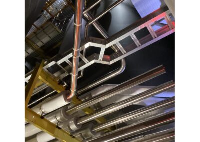 Custom galvanized ladder rack carrying cable alongside stainless process piping at the tank farm