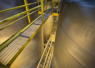Catwalk and galvanized cable tray running between stainless steel storage tanks in the tank farm